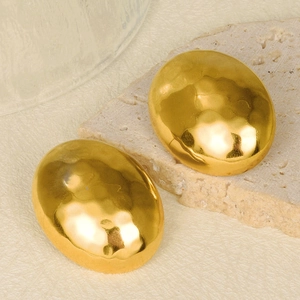 Macro shot of gold teardrop earrings with hammered texture on a natural stone surface