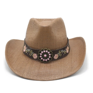 Detail of hand-woven straw cowboy hat featuring floral embroidery and bronze metal ornament