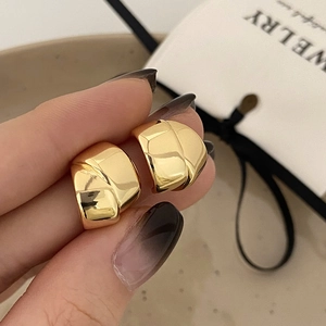 Close-up of chunky gold hoop earring with textured architectural design and mirror finish