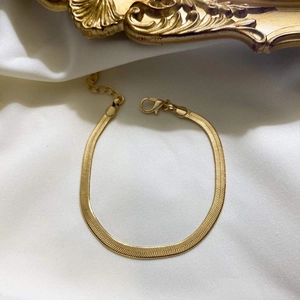 Detailed macro of golden flat snake chain bracelet with lobster clasp on white silk fabric