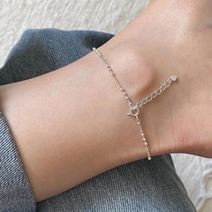Detail of minimalist S925 sterling silver beaded anklet with heart charm and extender chain