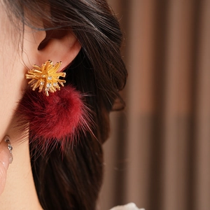 Detail of model wearing gold flower earrings with red pompon and sparkling zircon crystals