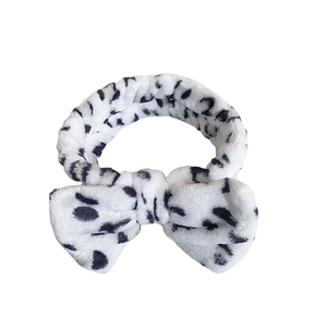 Plush white headband with black cow print and large bow knot for skincare use