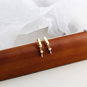 Detail view of gold stud earrings with pearls and zircon on a wooden box