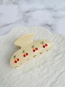Detail of cream acetate hair claw clip featuring sparkling red rhinestone cherries