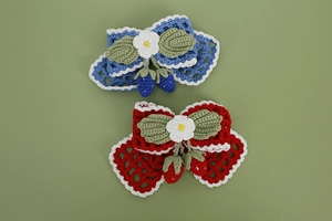 Detail of hand-crocheted strawberry bow hair clips in blue and red yarn on green background
