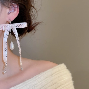 Detailed close-up of pink polka dot bow earrings with pearls on model side view