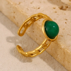 Macro shot of 18K gold plated chain ring with a green gemstone on textured stone