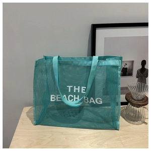 Detail showing mint green mesh beach bag with white THE BEACH BAG text on wooden desk