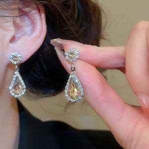 Detailed macro view of champagne teardrop crystal floral earrings worn by a model