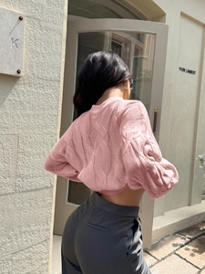 Outdoor shot of the back view of a pink cable knit cropped sweater with long sleeves