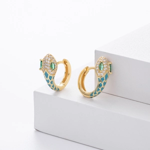 Detail of gold snake earrings with blue enamel scales and green oval gemstone eyes