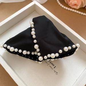 Détail d'une pince à cheveux noire en tissu avec perles élégantes sur plateau
