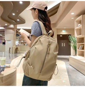 Close-up of beige nylon backpack featuring multiple pockets and woven zipper pullers