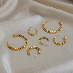 Detailed view of three sizes of gold-plated twisted C-shape hoop earrings on silk fabric