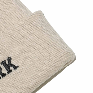 Close-up of beige ribbed knit beanie featuring detailed black RK letter embroidery