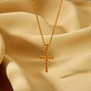 Detailed view of 18K gold beaded cross pendant on a fine chain over silk fabric