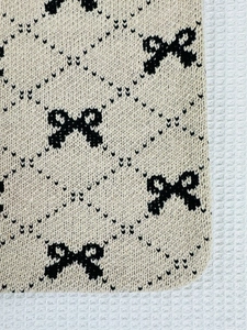 Detailed macro view of beige knitted fabric with black bow pattern and diamond texture