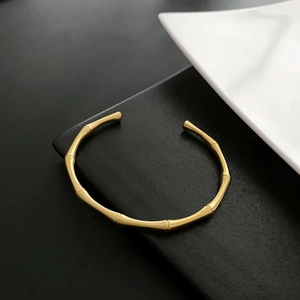 Detailed view of a golden bamboo-shaped open cuff bracelet on a minimalist tray