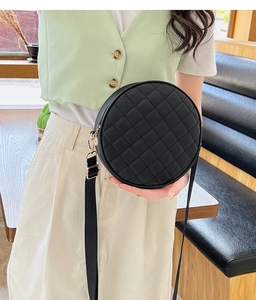 Detail of black round quilted crossbody bag with gold hardware and wide shoulder strap