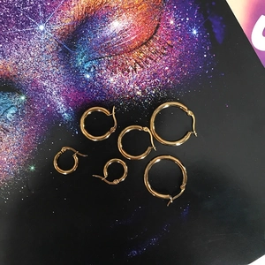 Three pairs of different sized gold titanium steel hoop earrings on a fashion magazine