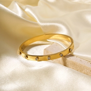 Polished 18k gold plated stainless steel bangle with sparkling zircons on stone surface