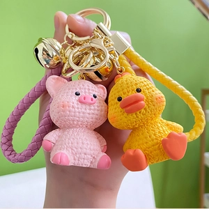 Close-up of cute pink pig and yellow duck keychains with woven texture and gold bells