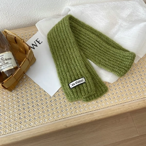 Detail of green knit scarf texture with a KN STUDIO label on a rustic rattan surface