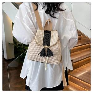 Detail view of woven straw backpack with black tassel charm and drawstring on stairs