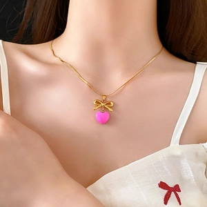 Gros plan du collier avec pendentif nœud doré et cœur rose porté par un mannequin