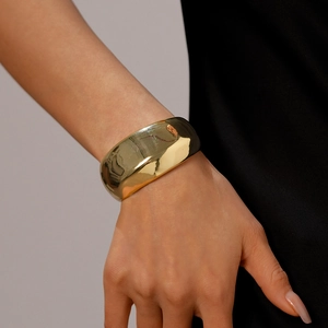 Close-up of polished gold-finished wide open cuff bracelet worn by a model