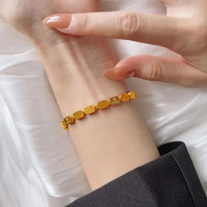 Detailed close-up of golden square link bracelet with LOVE engraving on silk fabric