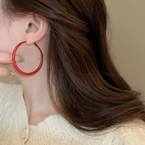 Detail of red oversized circular hoop earrings in lacquer finish on female model