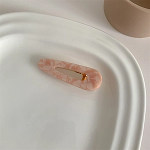 Detail of pink tortoiseshell acetate hair clip with golden metal fastener on ceramic tray