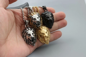 Hand holding 3D lion head necklaces in gold, silver, and black metal finishes