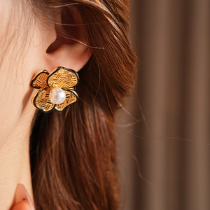 Close-up of a vintage gold flower earring with a pearl center and black edges on model
