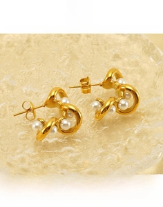 Detailed close-up of C-shaped titanium steel earrings with pearls on a textured tray