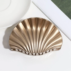 Detail shot of a golden shell-shaped hair claw clip with textured metallic finish