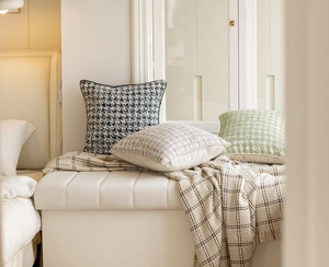 Detailed close-up of beige luxury cushions and a plaid blanket in a cozy living room setting