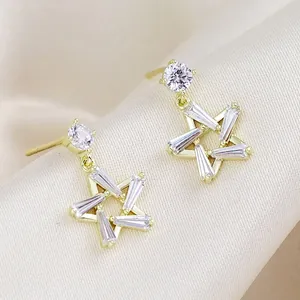 Vista macro de pendientes de estrella dorados con circonitas sobre una tela de seda beige