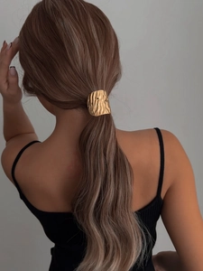Detail of a golden hammered metal hair ring accessory on a low ponytail hairstyle