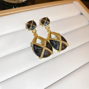 Detailed shot of golden bow earrings with black textured inlay on a white jewelry stand