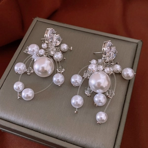 Macro shot of silver pearl drop earrings with sparkling zircon on a textured jewelry box
