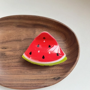 Detail of cute acrylic watermelon slice hair claw clip on an oval wooden tray