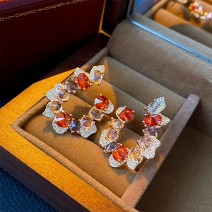 Macro shot of gold C-shape drop earrings with orange and purple gemstones in a jewelry box