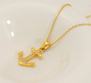 Detail of 18K gold plated anchor necklace pendant with micro-set zircon stones on white porcelain
