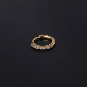 Macro detail of a small gold hoop earring with white cubic zirconia on black background