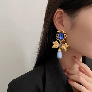 Close-up of a vintage golden bow earring with blue stones worn on a model's ear