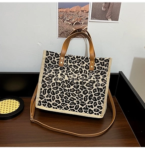 Leopard print burlap tote bag with brown PU leather handles and detachable strap on wood surface