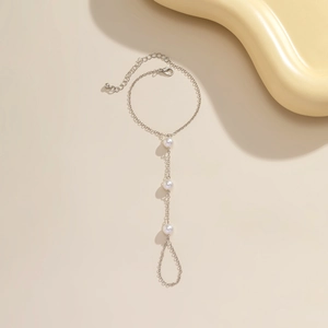 Detailed view of silver finish finger bracelet with three white pearls on beige surface